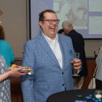 four people laugh around a cocktail round holding drinks at celebration event